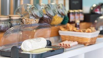 A buffet with various food items, including a covered cheese display, jars of condiments, and baskets of bread.