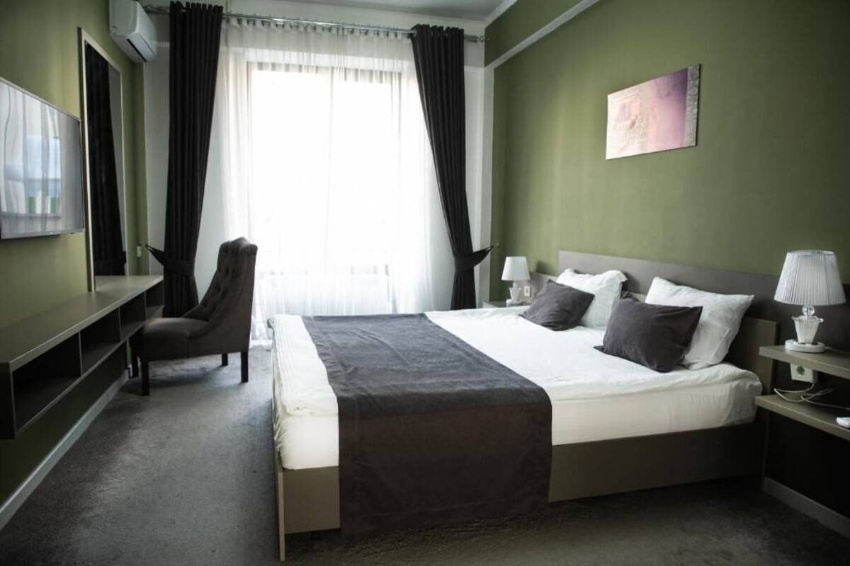 A hotel room with a bed, a chair, a desk, a lamp, and a painting on the wall.