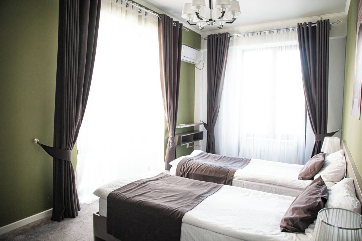 A hotel room with two beds, a ceiling fan, and a window with curtains.