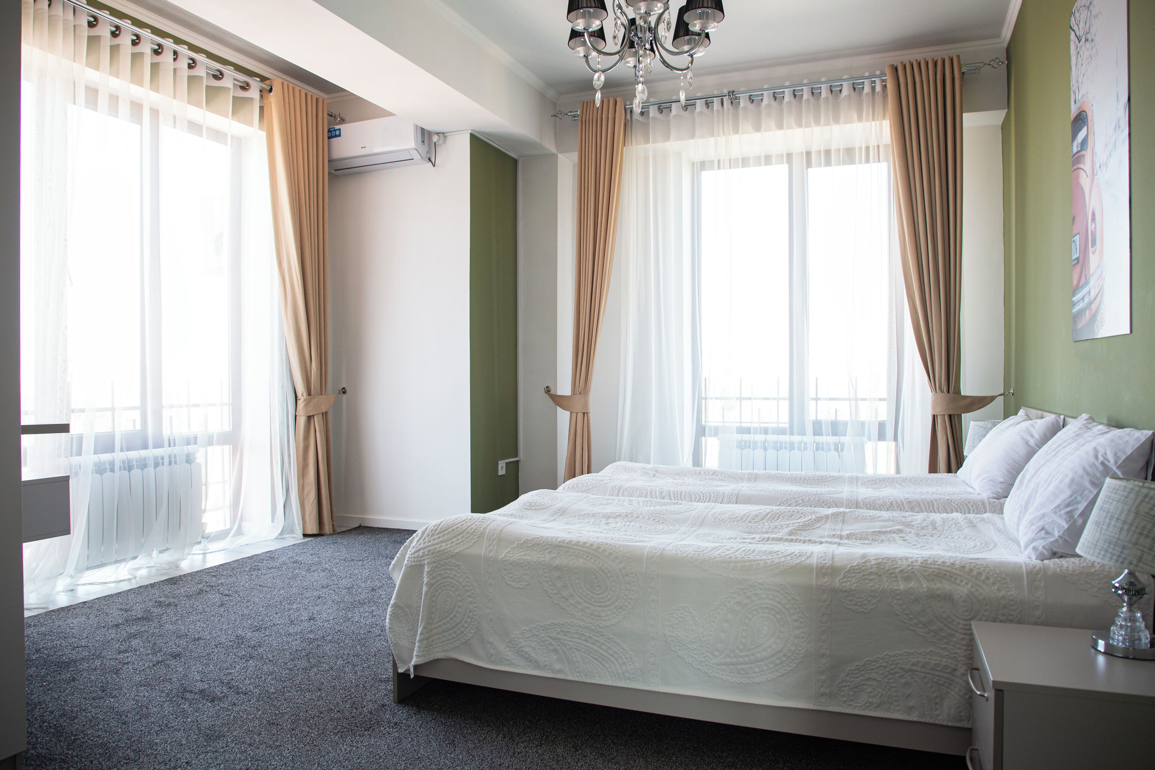 A hotel room with two beds, a chandelier, and large windows with curtains.