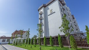 Un hotel moderno con techo plano, varios balcones y un césped bien cuidado con árboles jóvenes.