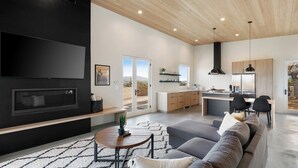 Ein modernes Wohnzimmer mit Flachbildfernseher, Kamin, einer Couch und einem Essbereich mit einer Küche im Hintergrund.