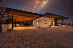 A modern house with a covered patio, a stone wall, and a view of the night sky.