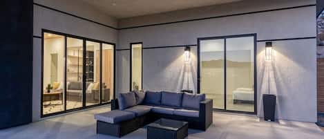 A modern outdoor living area with a sectional sofa, a coffee table, and a glass door leading to a bedroom.