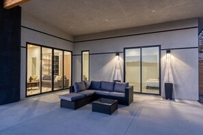 A modern outdoor living area with a sectional sofa, a coffee table, and a glass door leading to a bedroom.