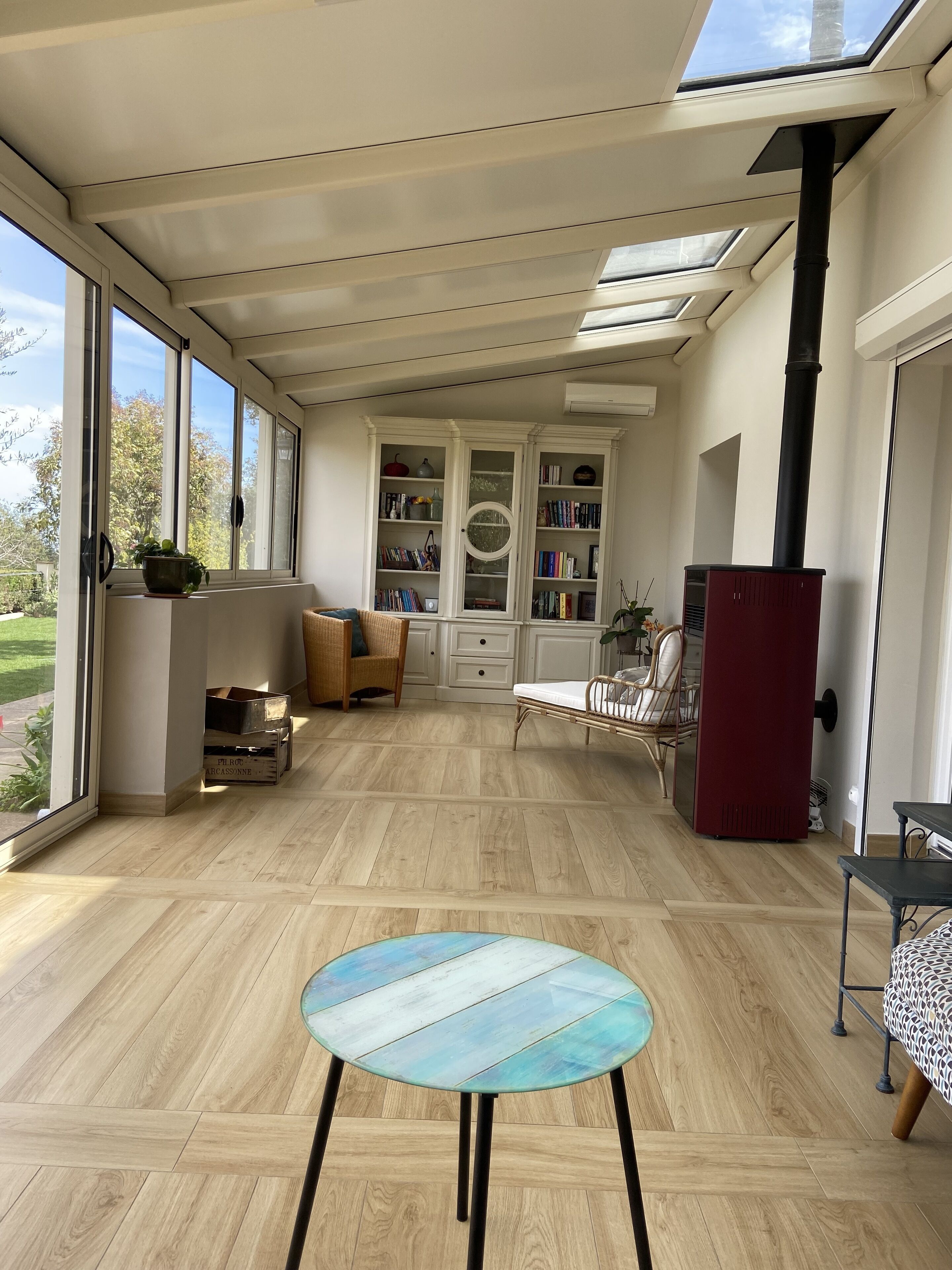 Il s'agit d'une pièce spacieuse avec un plafond haut, de grandes fenêtres et un puits de lumière. Le sol est en bois, il y a une table ronde et un buffet rouge.