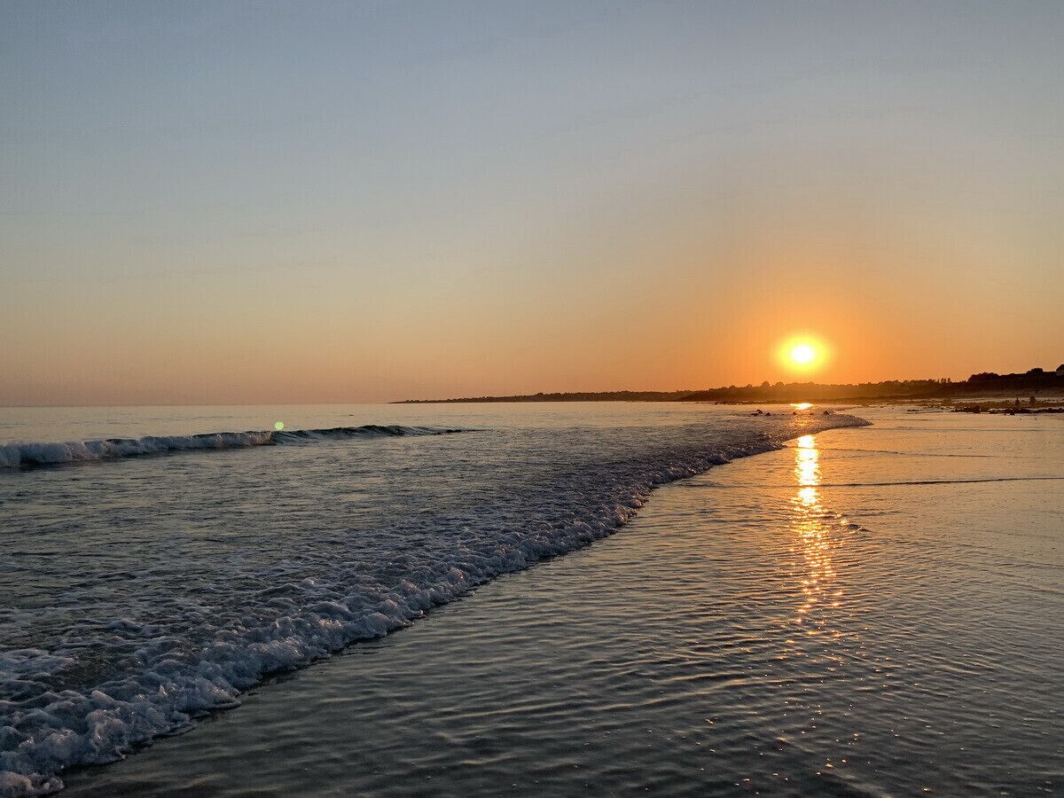 Ein Strand bei Sonnenuntergang, sanfte Wellen branden ans Ufer.