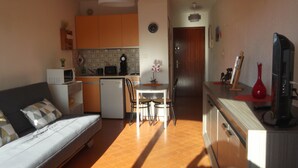 A compact living space with a sofa, kitchenette, dining area, and a TV. - Studio rental (Saint-Mandrier-sur-Mer)