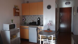 A compact kitchen with a microwave, toaster, and coffee maker. There is a dining table with two chairs and a potted orchid. - Studio rental (Saint-Mandrier-sur-Mer)