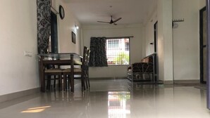 Une pièce spacieuse avec un plancher ciré, une table à manger avec des chaises, un lit avec un cadre en métal, un ventilateur de plafond et une fenêtre avec des rideaux.