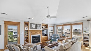 A spacious living room with a fireplace, comfortable seating, and large windows offering a view of the outside. - CheckMate: Walk to Beach, Large Pool, Hot Tub (Southern Shores)