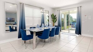 A modern dining area with a glass table, blue chairs, and a large potted plant. - Entertaining Retreat with Themed Bedrooms at Encore (Kissimmee)