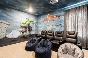 Une pièce décorée d’une fresque représentant des super-héros, avec des fauteuils en cuir noir et des poufs.
