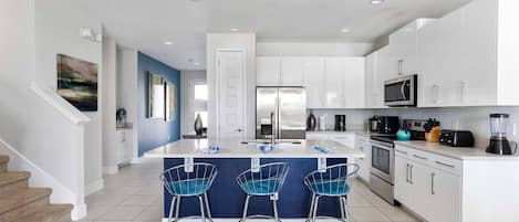 A modern kitchen with white cabinets, a central island with bar stools, stainless steel appliances, and a staircase leading to another level.