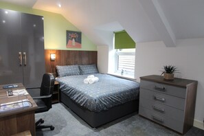 Een slaapkamer met een bed, bureau, stoel en een dressoir.