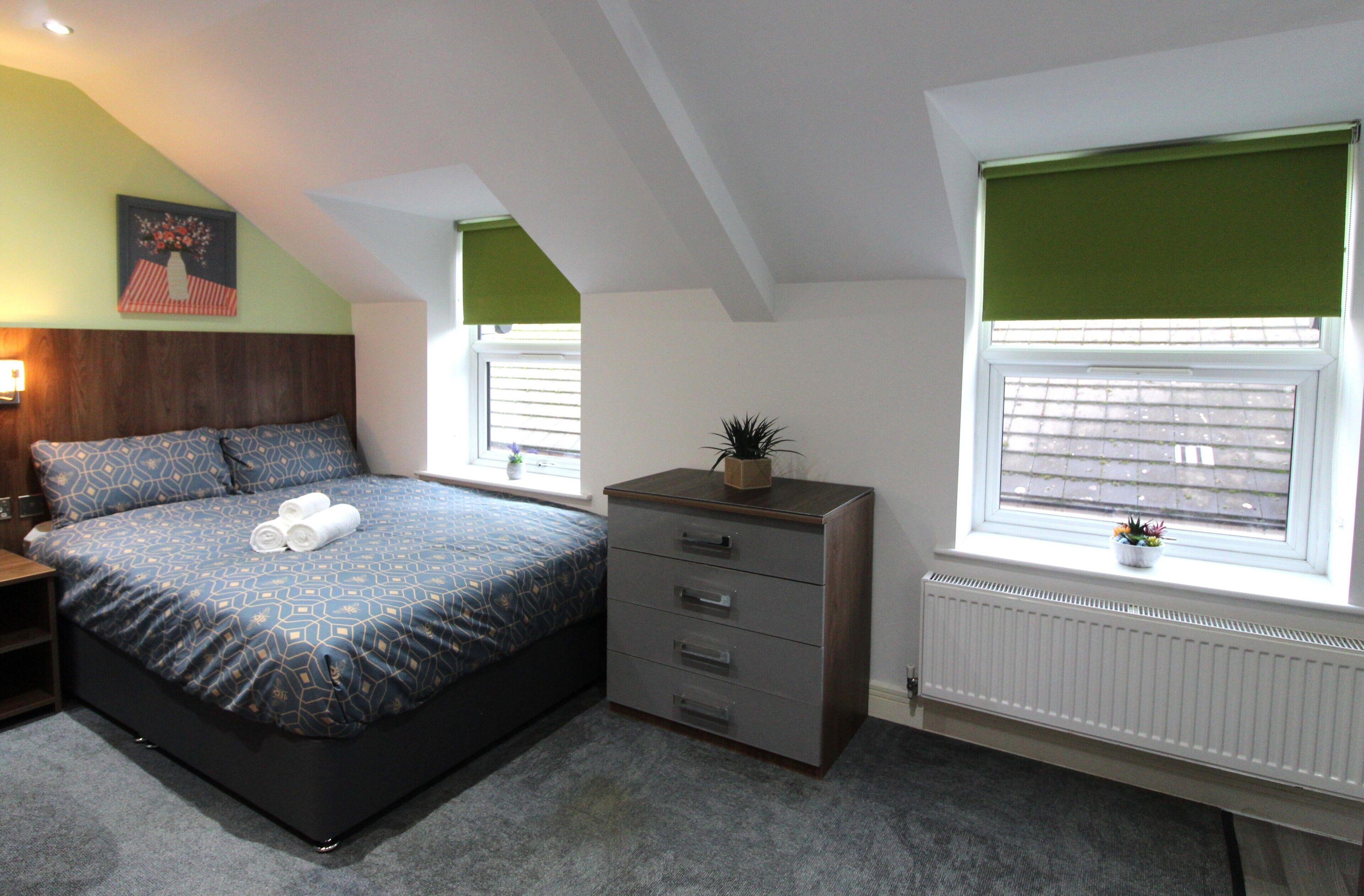 A bedroom with a bed, dresser, windows, and a radiator.
