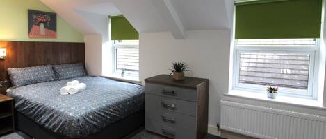 A bedroom with a bed, dresser, windows, and a radiator.