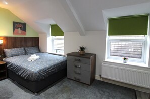 Een slaapkamer met een bed, een dressoir, ramen en een radiator.