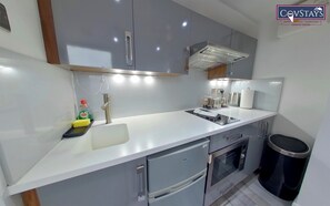 Een moderne keuken met grijze kastjes, een roestvrijstalen spoelbak, een inbouwoven en een prullenbak.