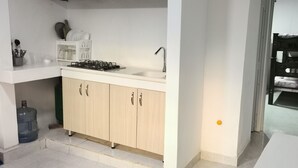 Eine kompakte Küche mit Gaskochfeld, Spüle und Holzschränken. Eine große Wasserspender befindet sich links.