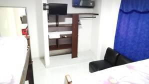 Ein Schlafzimmer mit einem Bett, einem Schreibtisch, einem Stuhl, einem Fernseher und einem blauen Vorhang.