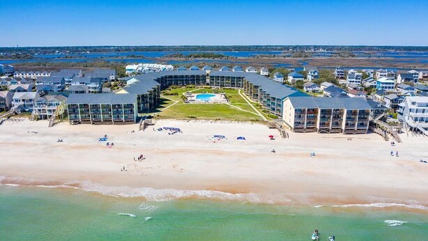 An aerial view of a coastal hotel with multiple buildings, a beach, and a pool area.