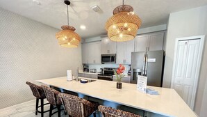 A modern kitchen with a large island, bar stools, and wicker pendant lights. - Bodacious Oasis - Private Pool, Free BBQ Grill! (Champions Gate)