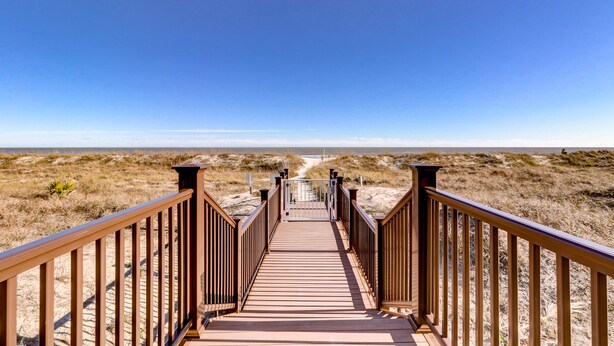 A wooden boardwalk leading to a beach with a clear blue sky.