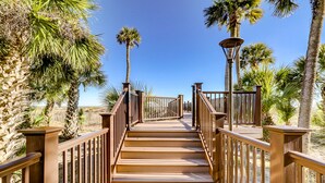 A wooden boardwalk with railings, leading towards palm trees and a clear blue sky.