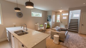Una cocina moderna con una isla grande, un comedor con mesa de vidrio y una escalera que sube a otro nivel.