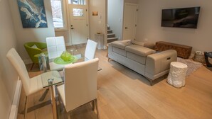 Una sala de estar moderna con una mesa de comedor de vidrio, un sofá gris y un televisor montado en la pared.