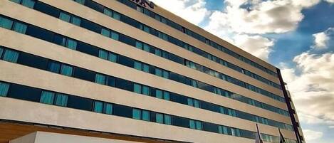 Un hotel moderno con franjas horizontales beige y azules, amplias ventanas y un cielo despejado con nubes.