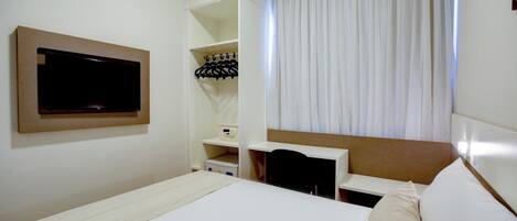 Habitación de hotel con cama, televisor montado en la pared, escritorio con silla y ventana con cortinas.