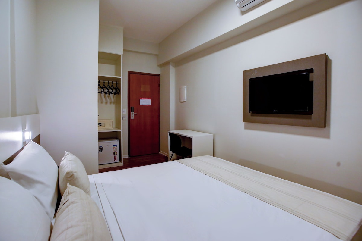 A hotel room with a bed, a desk, a TV, and a door leading to a bathroom.