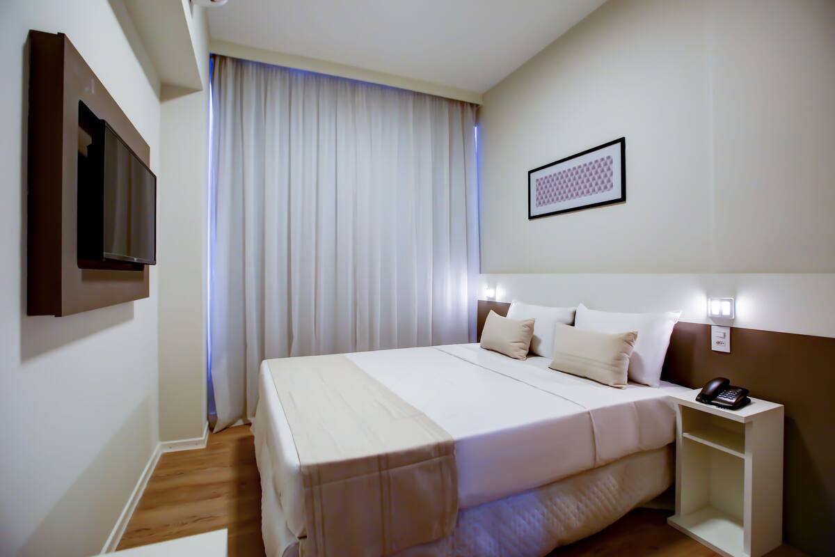 A hotel room with a bed, bedside table, and a mounted TV.