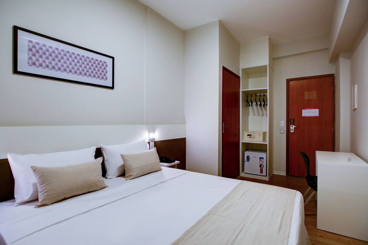 A hotel room with a bed, bedside table, lamp, wardrobe, and a coat rack.