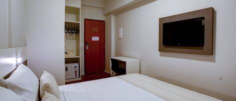 Habitación de hotel con cama, escritorio, televisión y puerta que da a un baño.