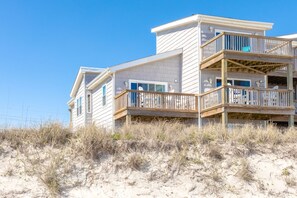 Een strandhuis met meerdere balkons en een zandig voorgrondgebied.
