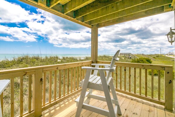 Une terrasse en bois avec une chaise blanche, donnant sur une plage sous un ciel dégagé.