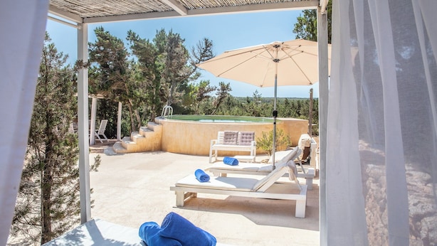 Zona junto a la piscina con sillones reclinables, piscina y pérgola.