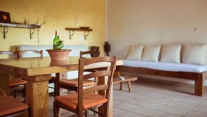 Un comedor con una mesa y sillas de madera, una planta en maceta y un sofá al fondo.