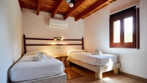 Un dormitorio con dos camas, vigas de madera en el techo, un equipo de aire acondicionado y una ventana con persianas.