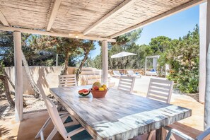 An outdoor patio with a wooden table and chairs, a fruit bowl, and a white umbrella. - Rustic House (Formentera)