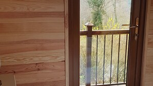 Ein Schlafzimmer mit Holzbalkendecke, einem Bett mit weißer Bettwäsche und einem Blumenkissen sowie einem Balkon mit Geländer und Blick auf Bäume und Berge.