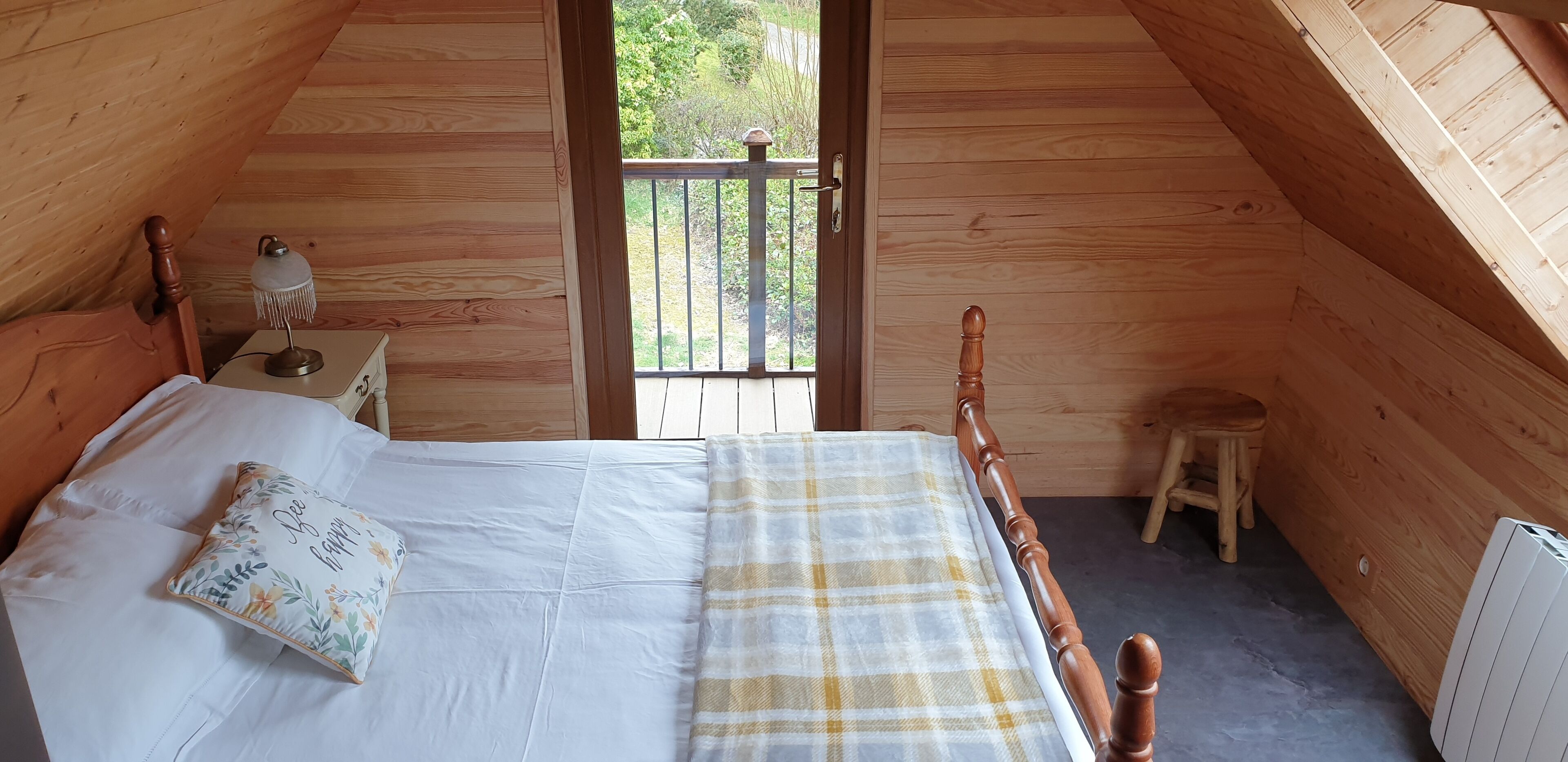Um quarto acolhedor de madeira com uma cama, uma mesa de cabeceira, um abajur e vista para o exterior através de uma porta.