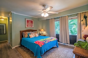Un dormitorio con cama, ventilador de techo, ventana con cortinas y vistas a zonas verdes.