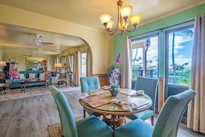 Un salón amplio con comedor, ventanas grandes y vistas a palmeras.