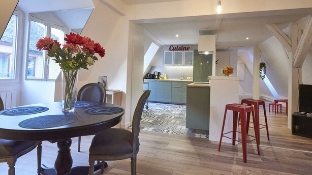 A dining area with a round table, chairs, and a vase of flowers. There is a kitchen area with a countertop and cabinets in the background. - Apartment SAINT-MARTIN2, in the heart of Colmar (Colmar)