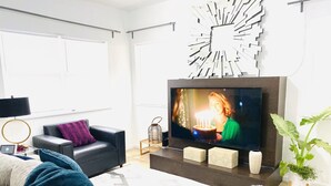 Un soggiorno moderno con una TV a schermo piatto, un divano in pelle nera, una coperta blu e un elemento decorativo a parete.