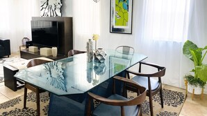 Un soggiorno moderno con un tavolo da pranzo in vetro, sedie di legno, una TV a schermo piatto, uno specchio decorativo e un grande quadro astratto.